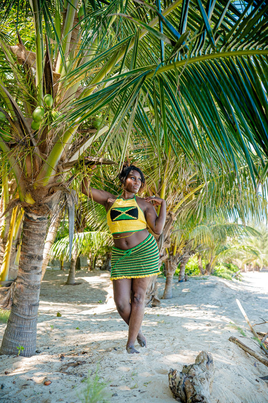 A person standing under palm trees wearing a green and yellow striped Jamaica top and skirt