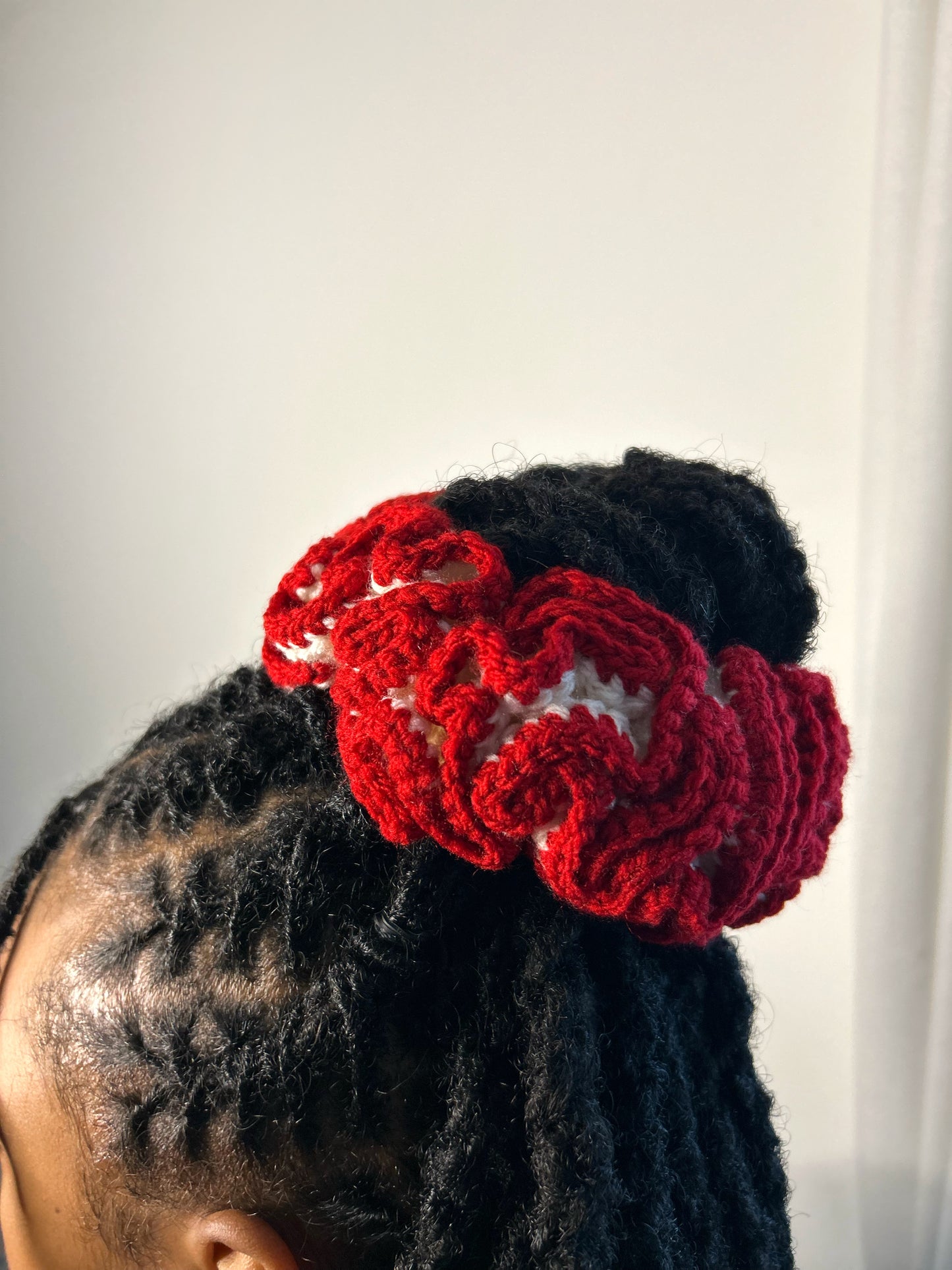 Red and cream crochet hair accessory on a person's head against a plain background