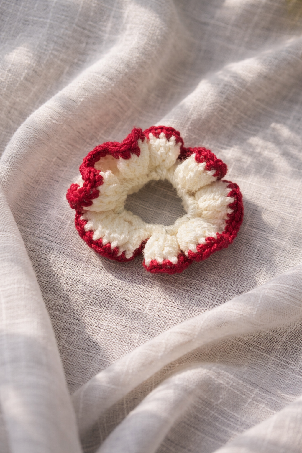 Crocheted scrunchie with red and white pattern on a textured beige fabric background