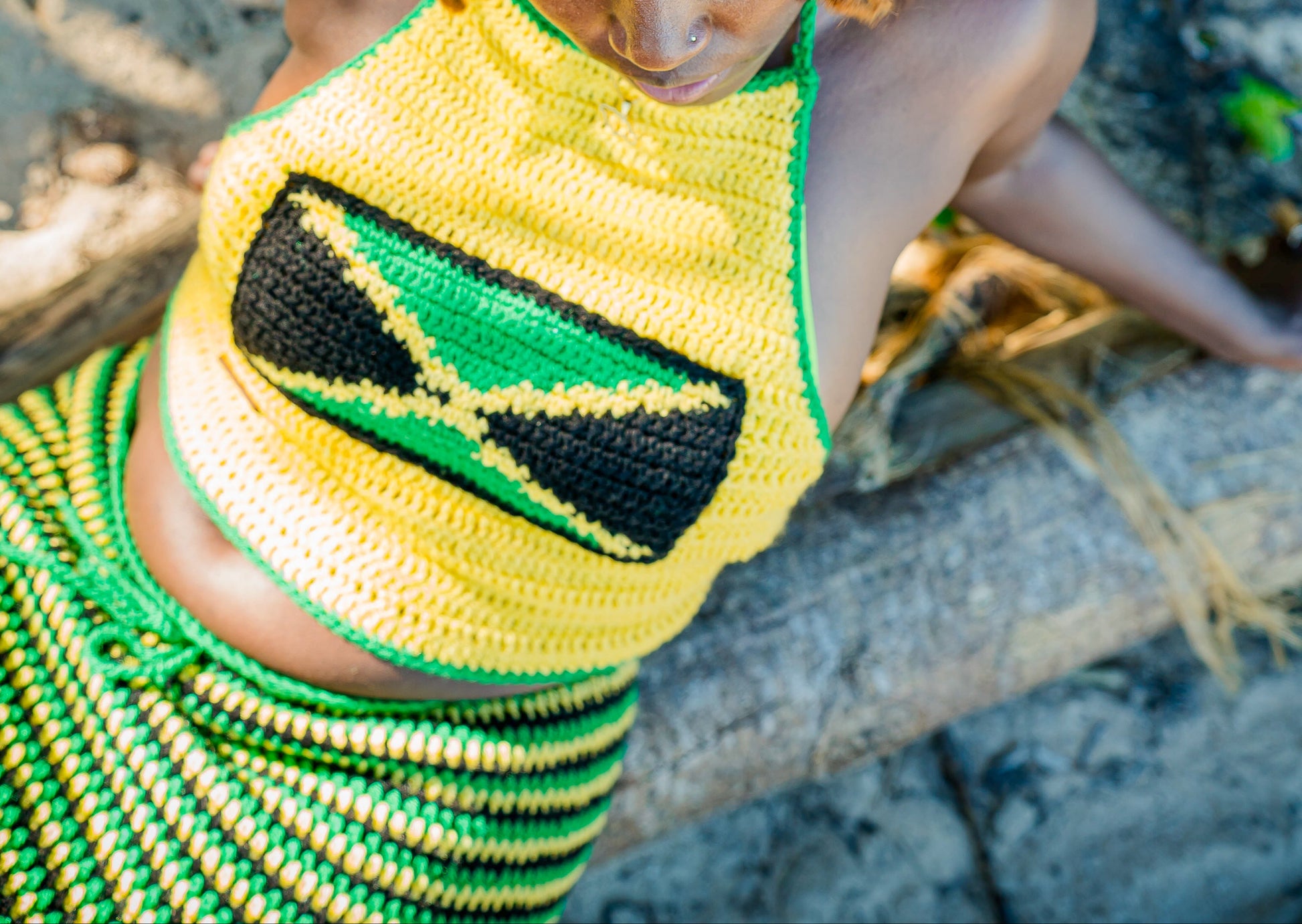 a women wearing a jamaica flag top with green, black and yellow skirt sitting on a branch on the beach 